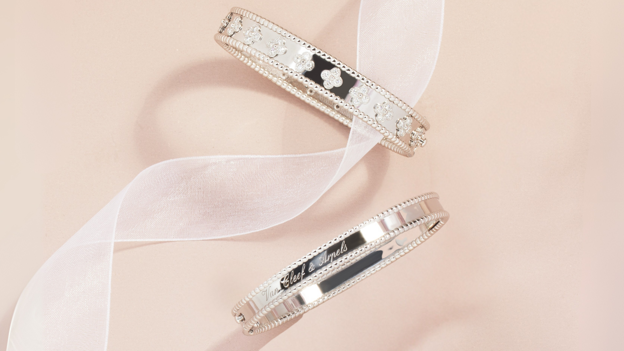 Two Van Cleef bangle bracelets on a light pink background