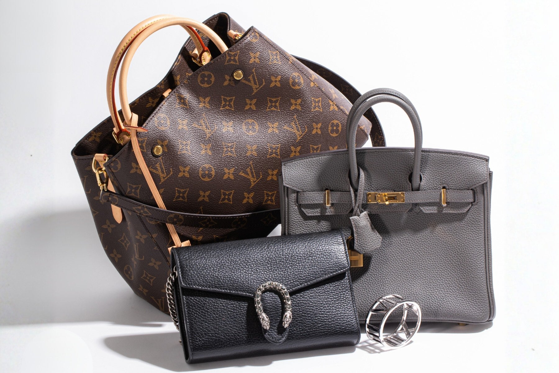 Three handbags including a brown Louis Vuitton bag, a black Gucci bag, and a gray bag on a white background