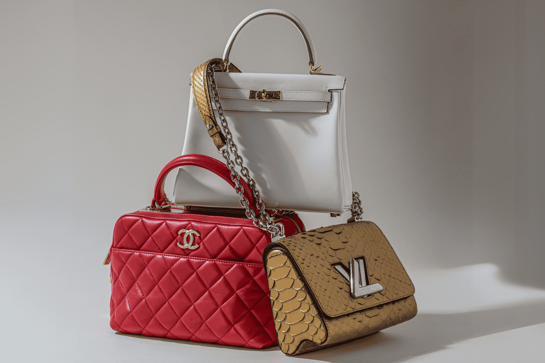 Three designer handbags in red, white and gold on a white background