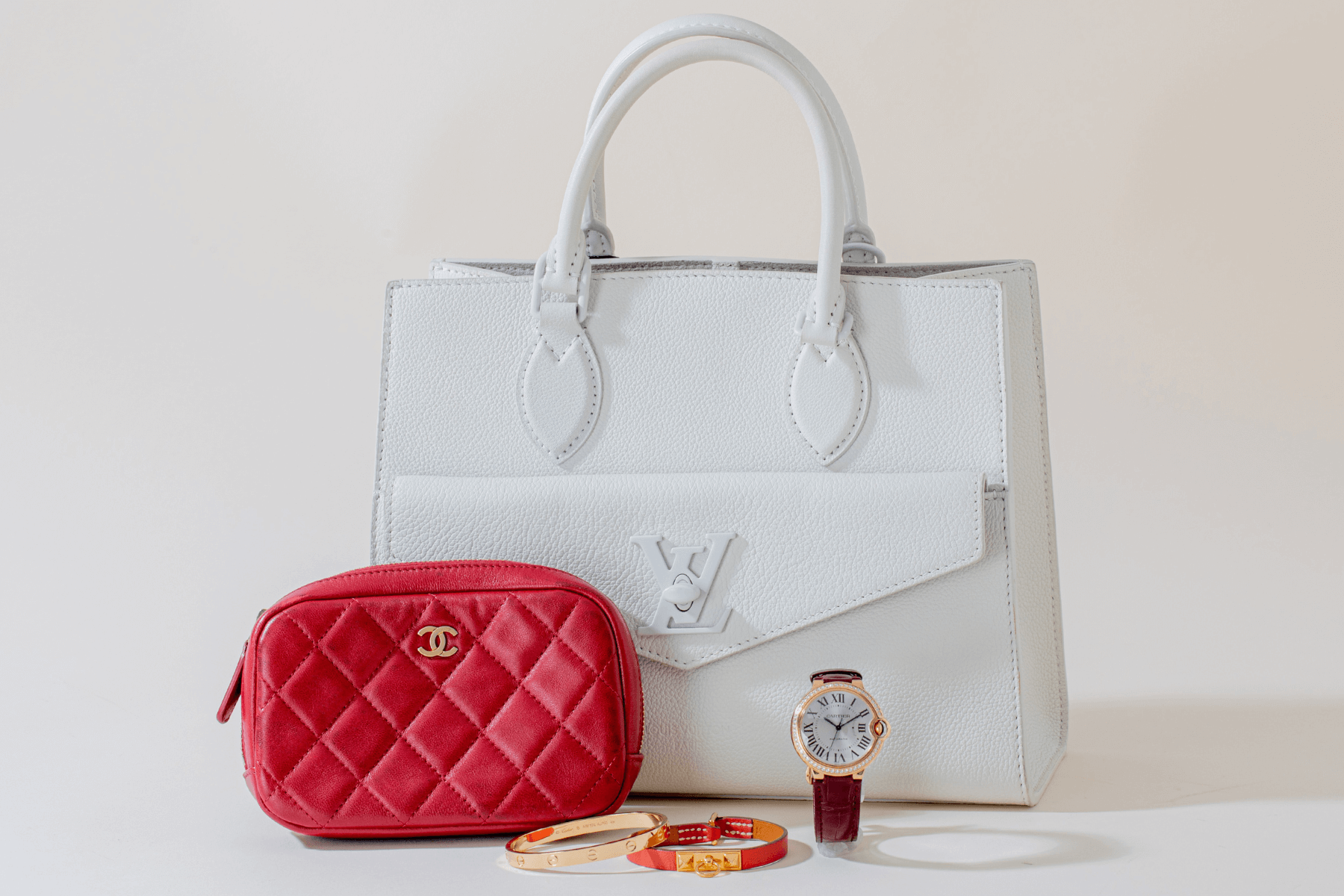 White Louis Vuitton handbag, red quilted Chanel pouch, and watch on a light background