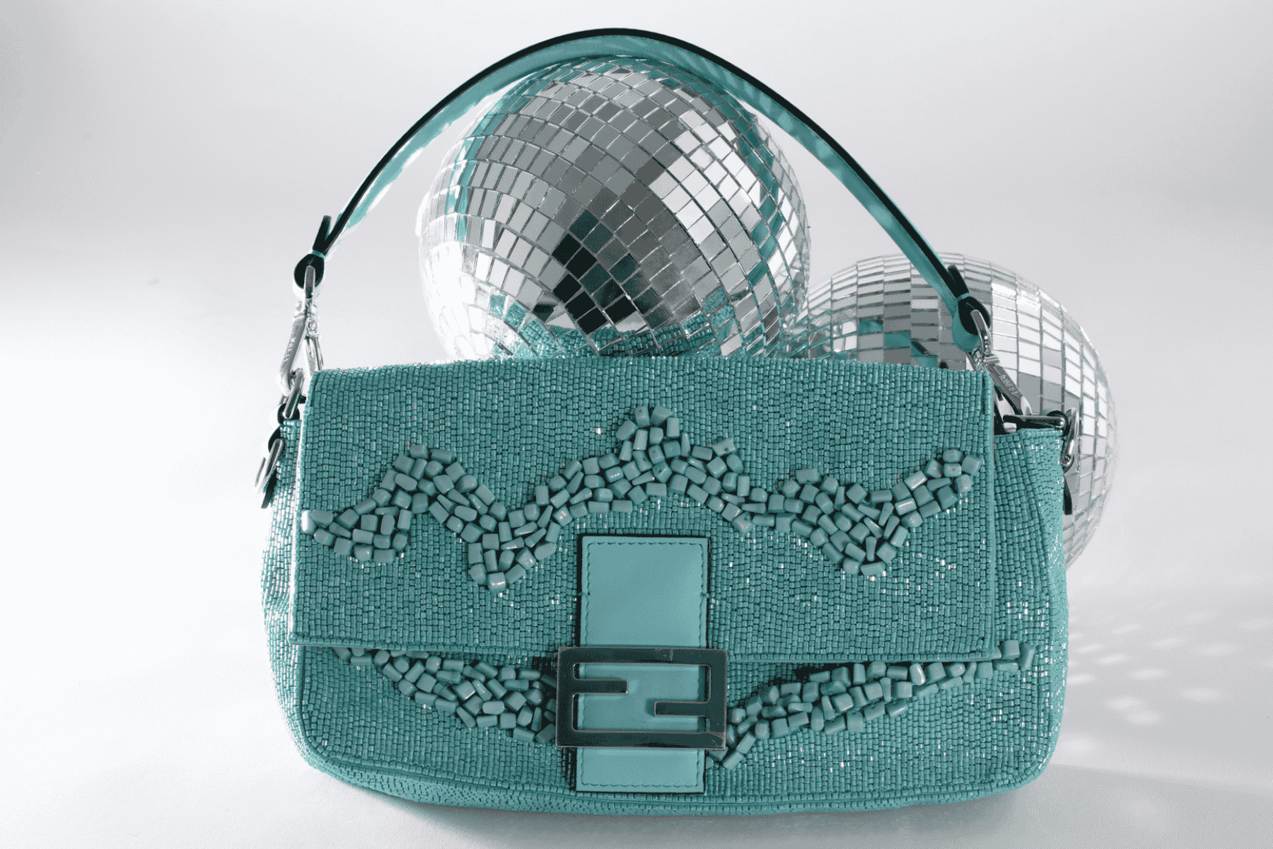 Turquoise Fendi Baguette bag with decorative patterns and a mirror ball on a white background