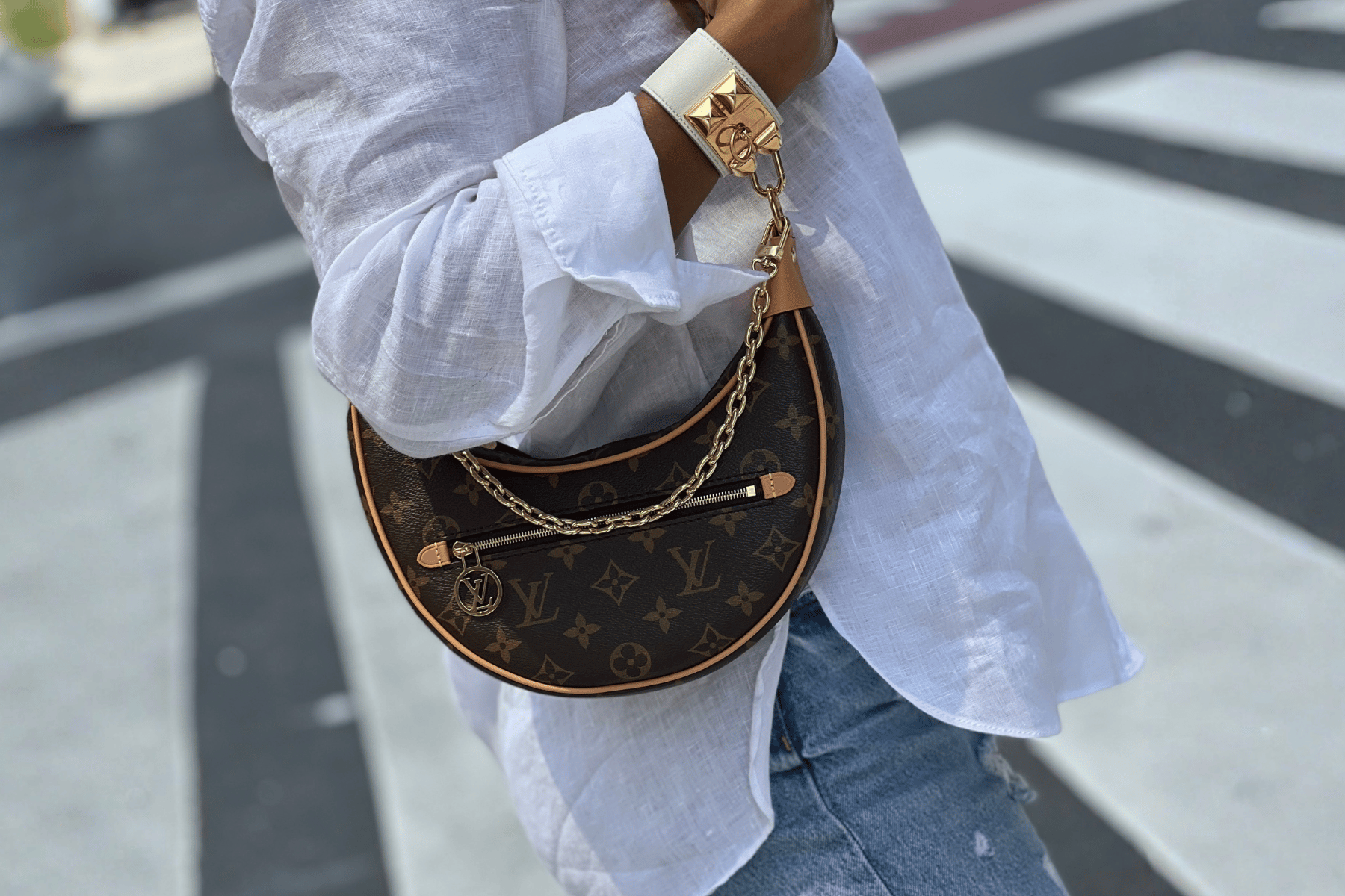 Person wearing a white shirt and blue jeans with a brown Louis Vuitton handbag featuring gold chain details.